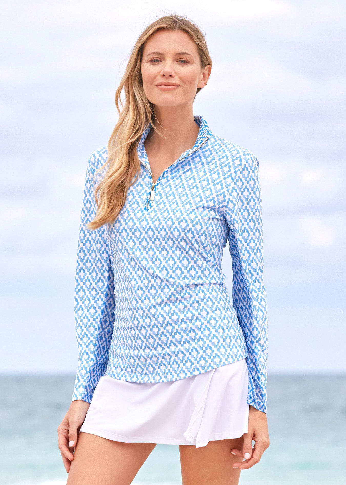 A blonde woman on the beach wearing the Cabana Life sun protective Seaside 1/4 Zip Sport Top and White Classic Swim Skirt.