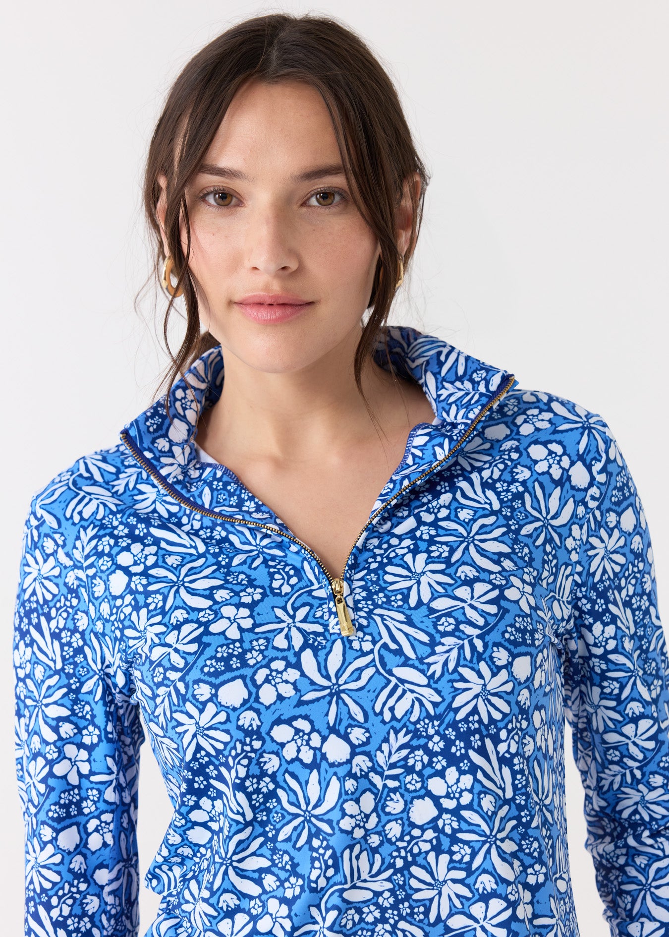 A dark haired woman wearing the Cabana Life sun protective Seaside Floral 1/4 Zip Sport Top with gold hoops.