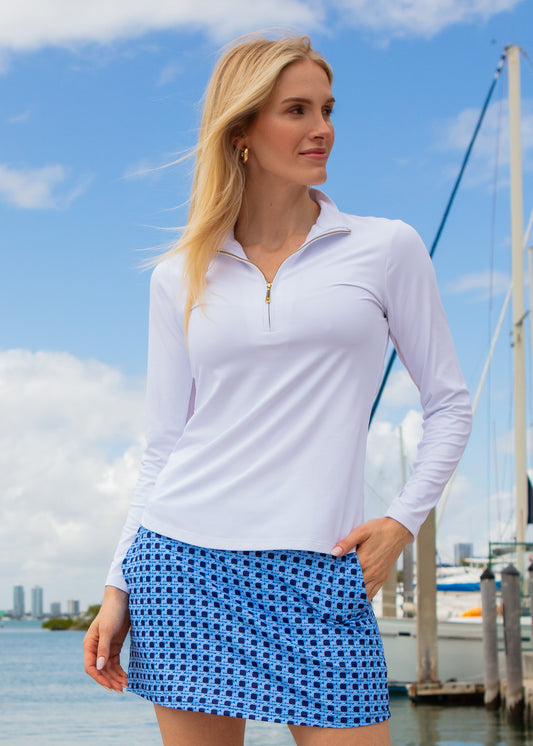 Woman wearing a white long-sleeve shirt and blue basketweave skirt by a marina.
