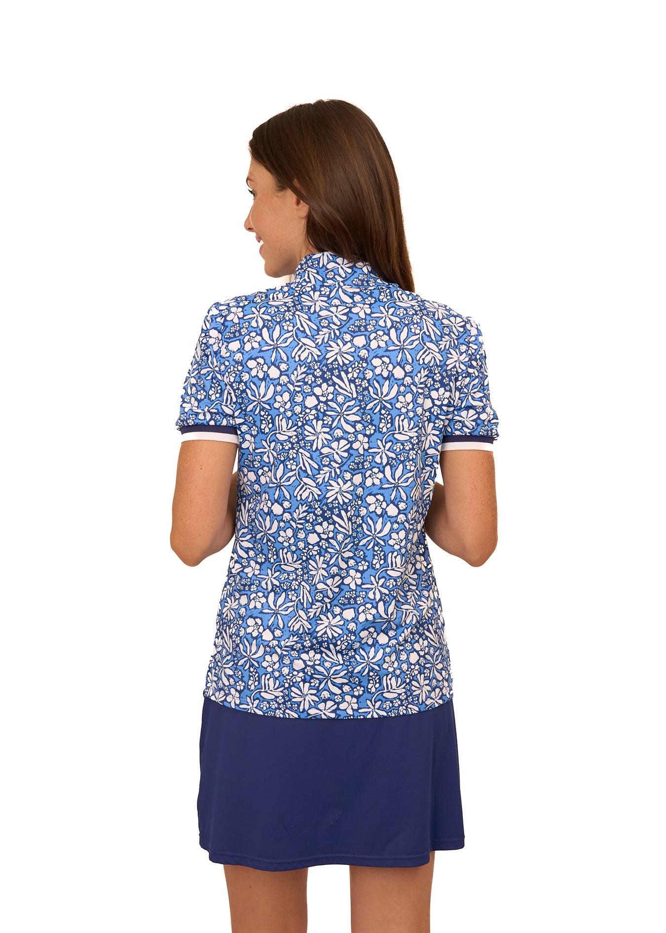 The back of a brunette woman wearing the sun protective & navy floral Seaside Short Sleeve Collared 1/4 Zip and Navy Skort from Cabana Life on a white background.