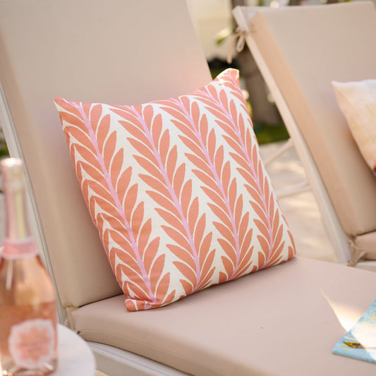 Decorative pillow with a pink leaf pattern on a beige chair.
