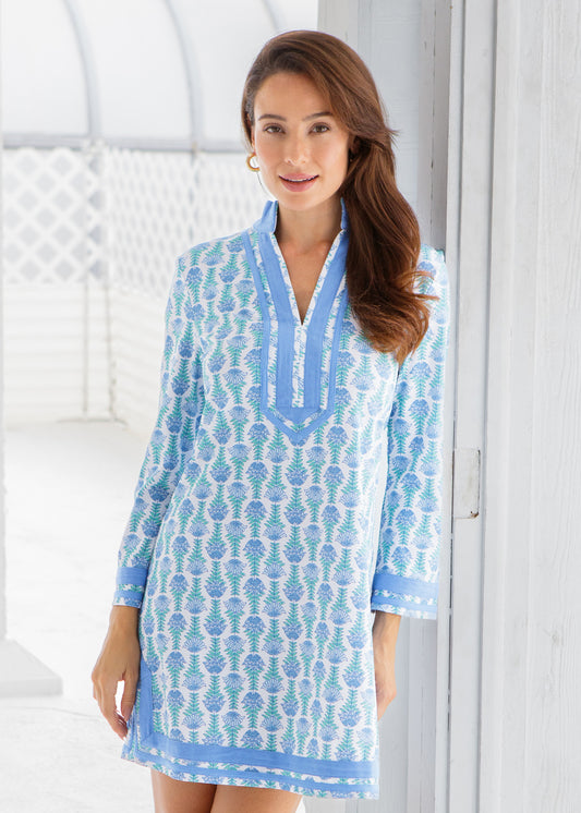 Woman wearing a blue patterned dress standing in a room with white walls .