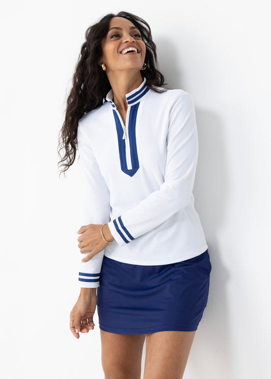A brunette woman wearing the Cabana Life White Collared 1/4 Zip with the Navy 15" Skort in a studio laughing.