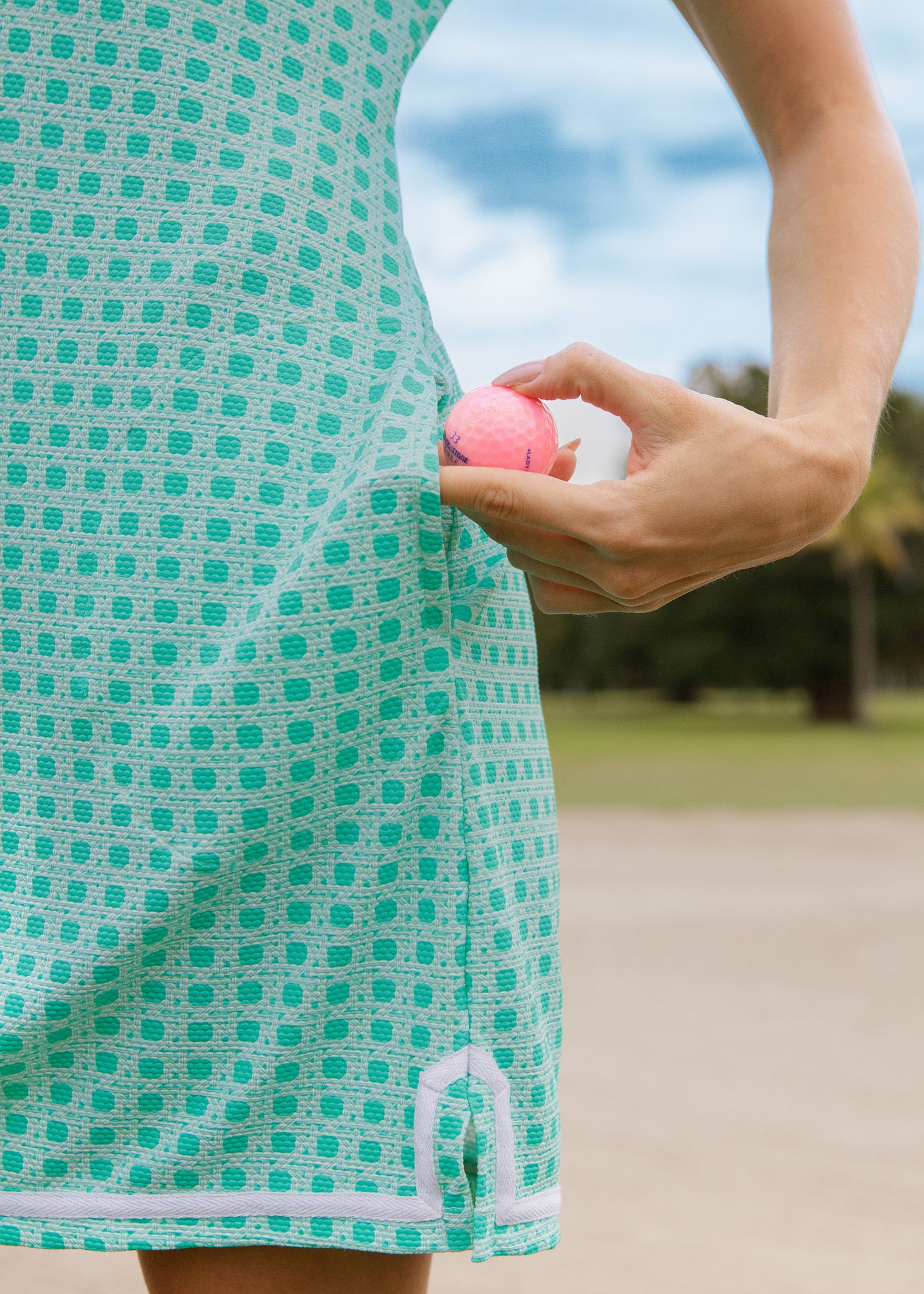 Person holding a pink golf ball wearing a green basketweave dress 