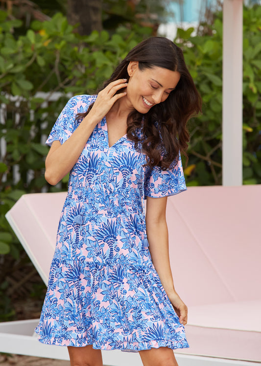 Woman wearing a blue floral dress sitting on a white bench with greenery in the background