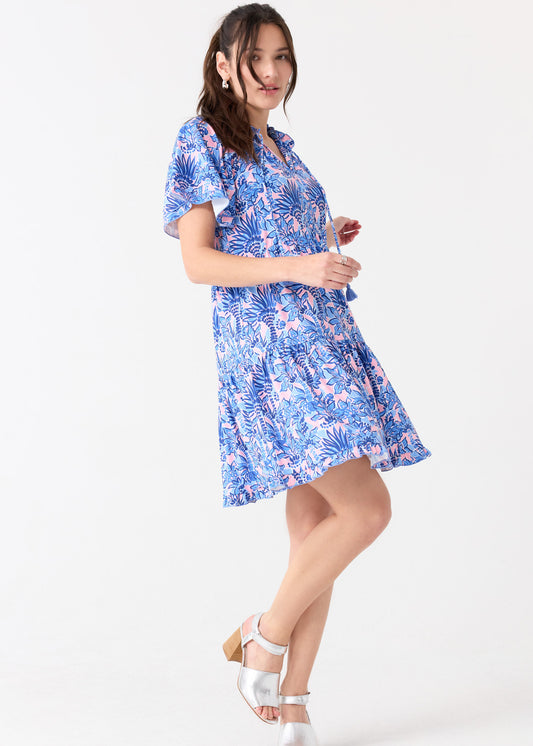 A brunette woman turning to the side in the flowy Cabana Life sun protective Palm Beach Short Sleeve Tiered Dress, paired with silver sandals.
