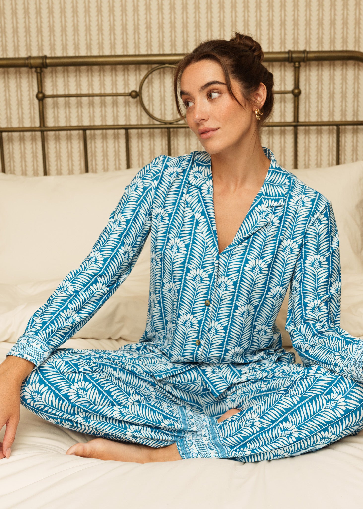 Woman sitting on a bed with white sheets, wearing our Harbor blue patterned sleep to street pajama set on a white background.