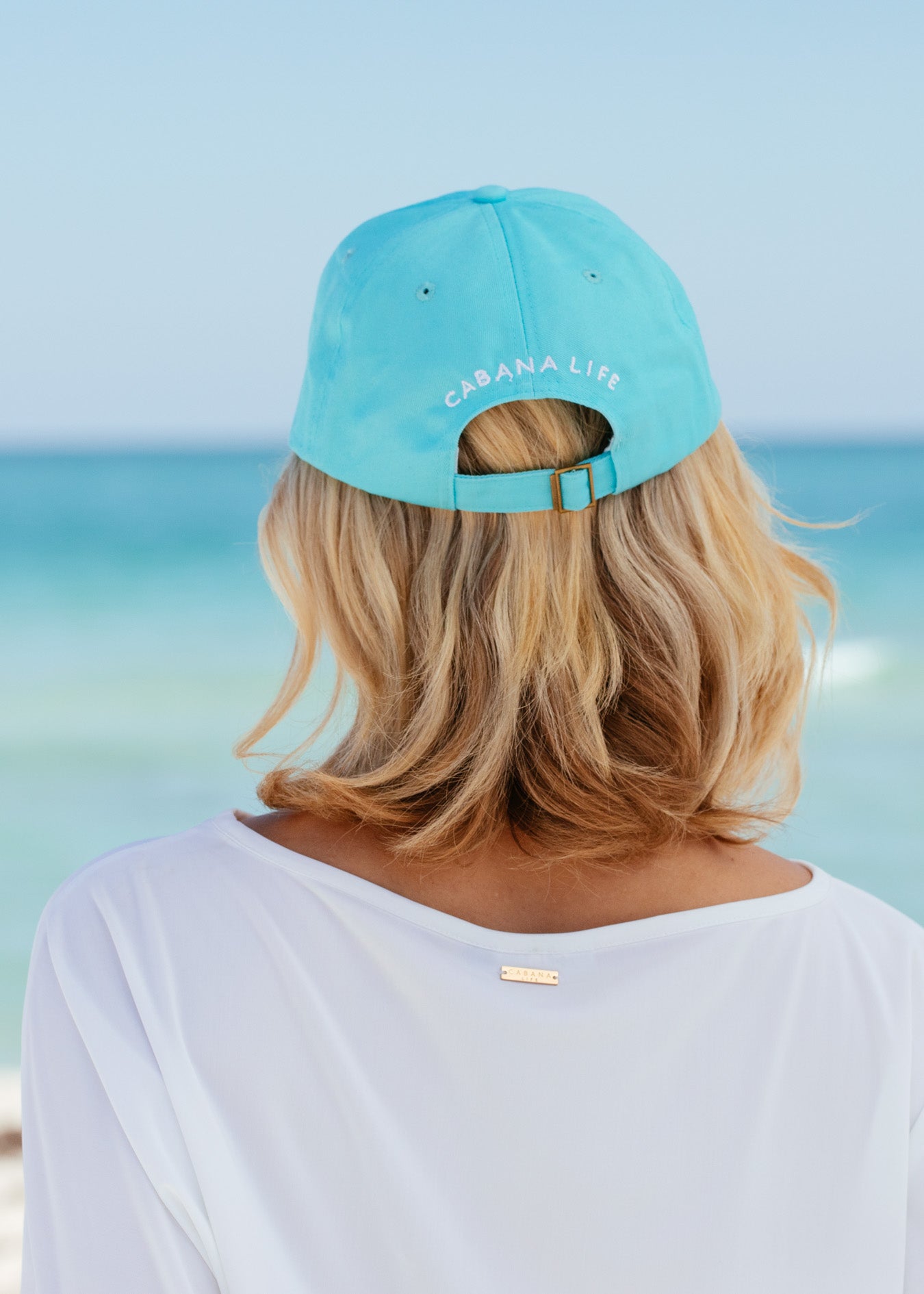 Back of blonde woman wearing Aqua Cabana Life Baseball Hat with white rashguard