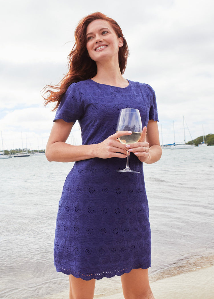 A redhead woman looking to the side and holding a glass of white wine while wearing the Navy Eyelet Short Sleeve Shift Dress on the sand.