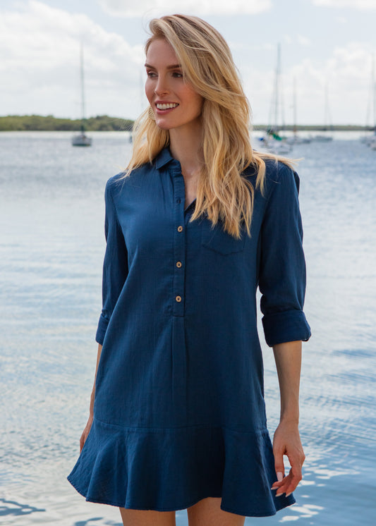 Woman wearing a blue dress standing by a waterfront with sailboats in the background