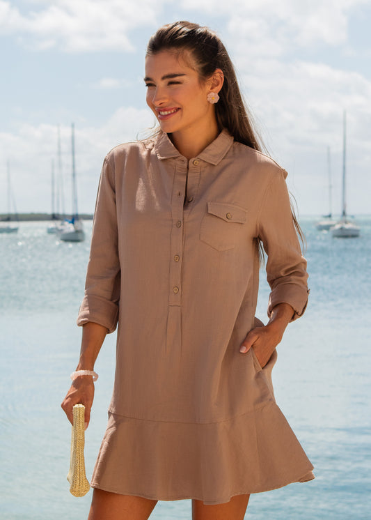 Woman in a khaki dress holding a straw bag with sailboats in the background