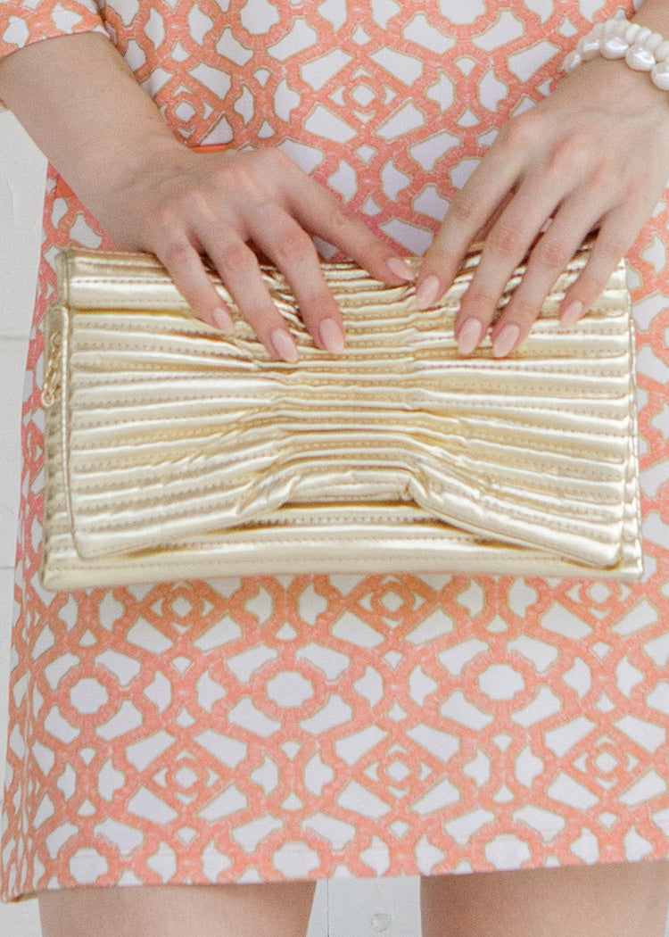Gold clutch held by a person wearing a patterned dress.