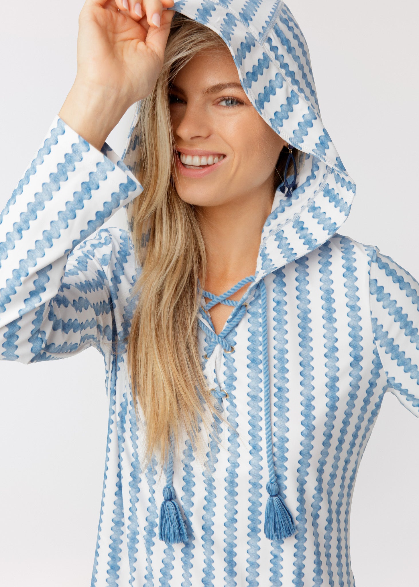 Woman wearing a blue and white striped cover up with tassels on a light background