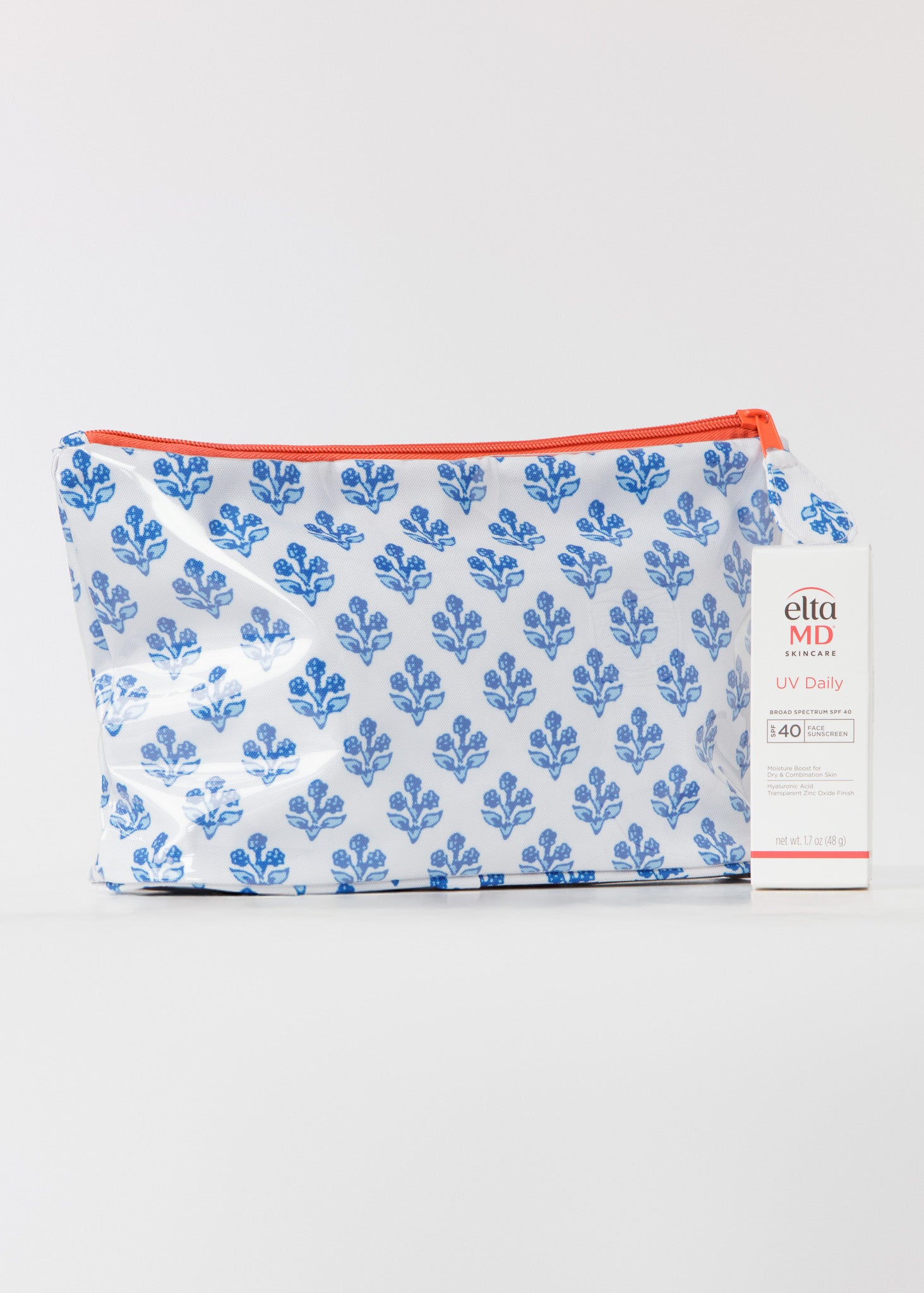 Small accessory bag with blue floral pattern and orange zipper on a white background with a box of SPF in front.