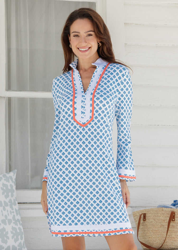Woman wearing a blue patterned dress with orange trim on a porch.