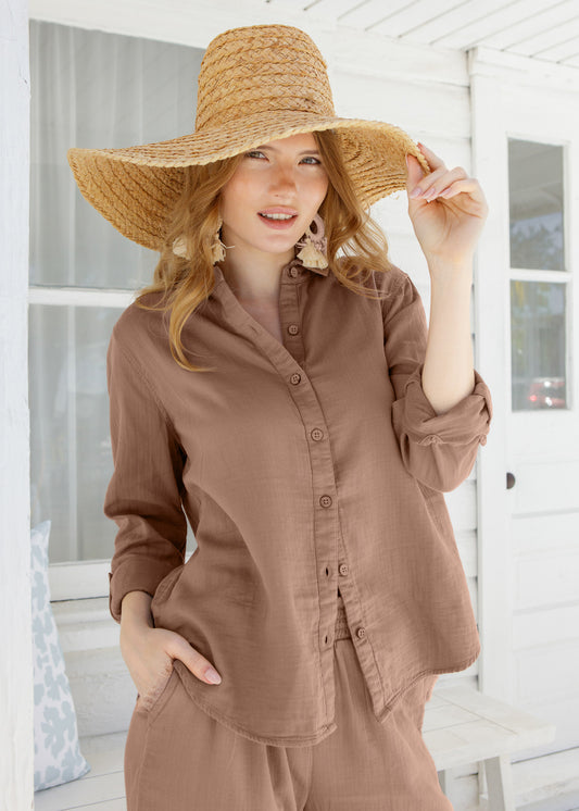 Woman wearing a brown outfit and straw hat on a white porch.
