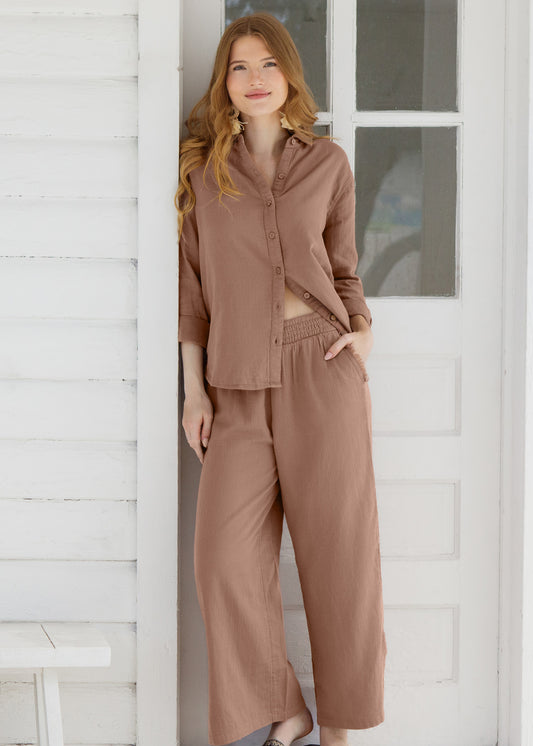 Woman wearing a brown outfit standing against a white wall.
