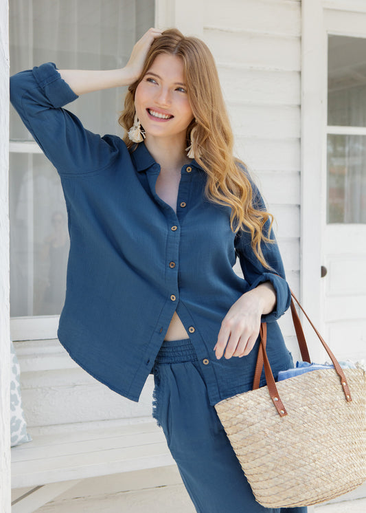 Woman in a blue outfit holding a straw bag on a porch.