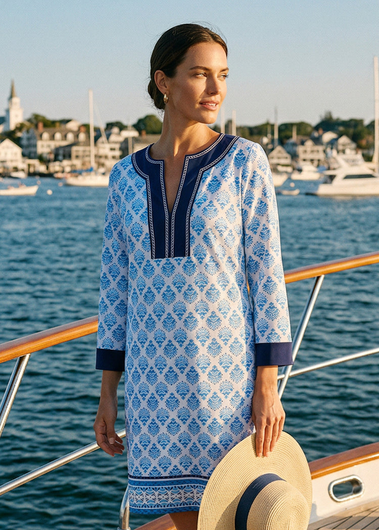 Woman in a blue and white patterned dress standing on a boat with a harbor in the background
