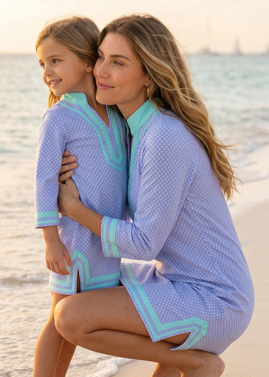 Woman and child wearing matching blue and green dresses on a beach.