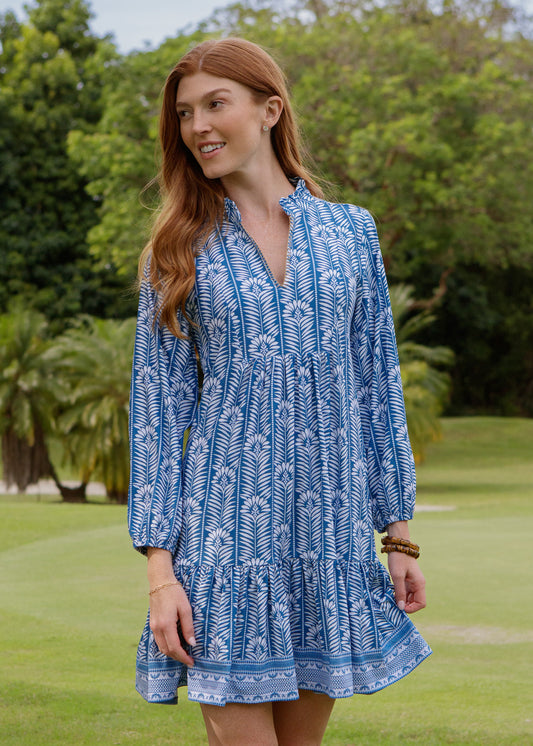 Woman wearing a blue patterned dress standing on a grassy area with trees in the background