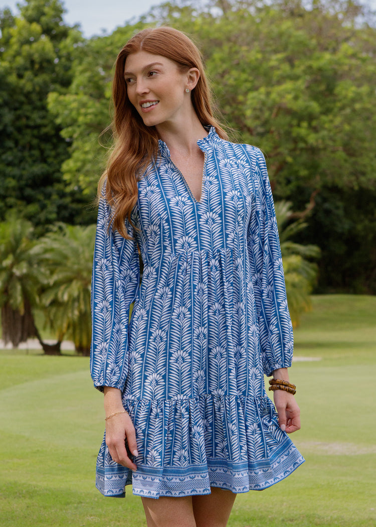 Woman wearing a blue patterned dress standing on a grassy area with trees in the background