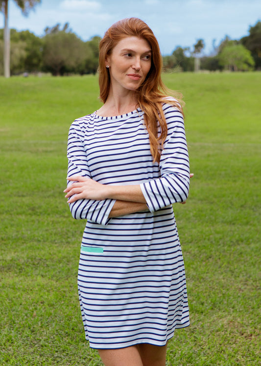 Woman wearing a striped dress standing in a grassy field with trees in the background