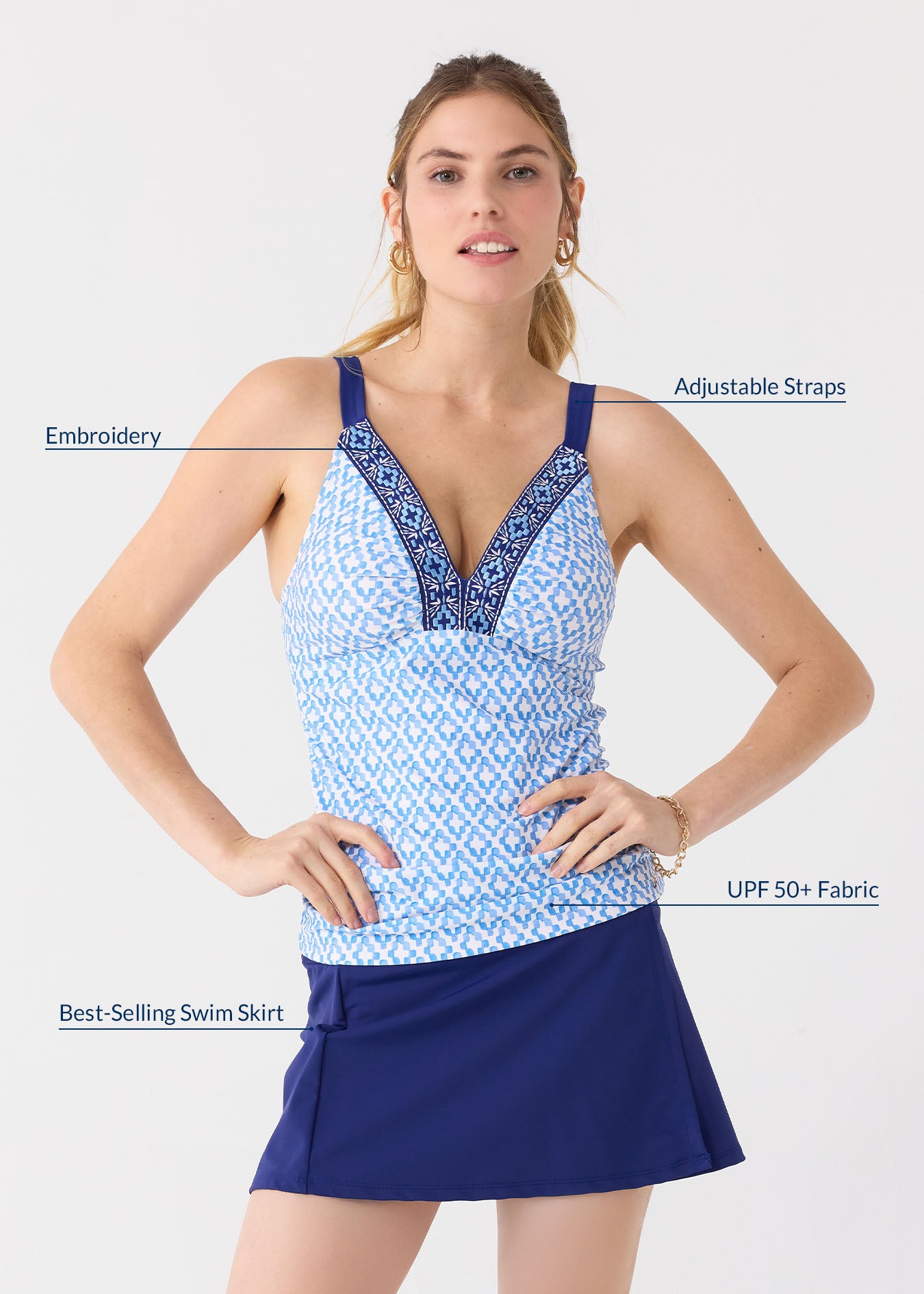 A blonde woman with hands on her hips wearing gold jewelry with the Cabana Life sun protective Seaside Embroidered Tankini Top and Navy Classic Swim Skirt.