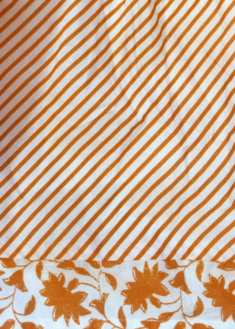 A close-up of a white fabric with diagonal orange stripes across most of the surface and a matching orange floral border along the bottom edge.