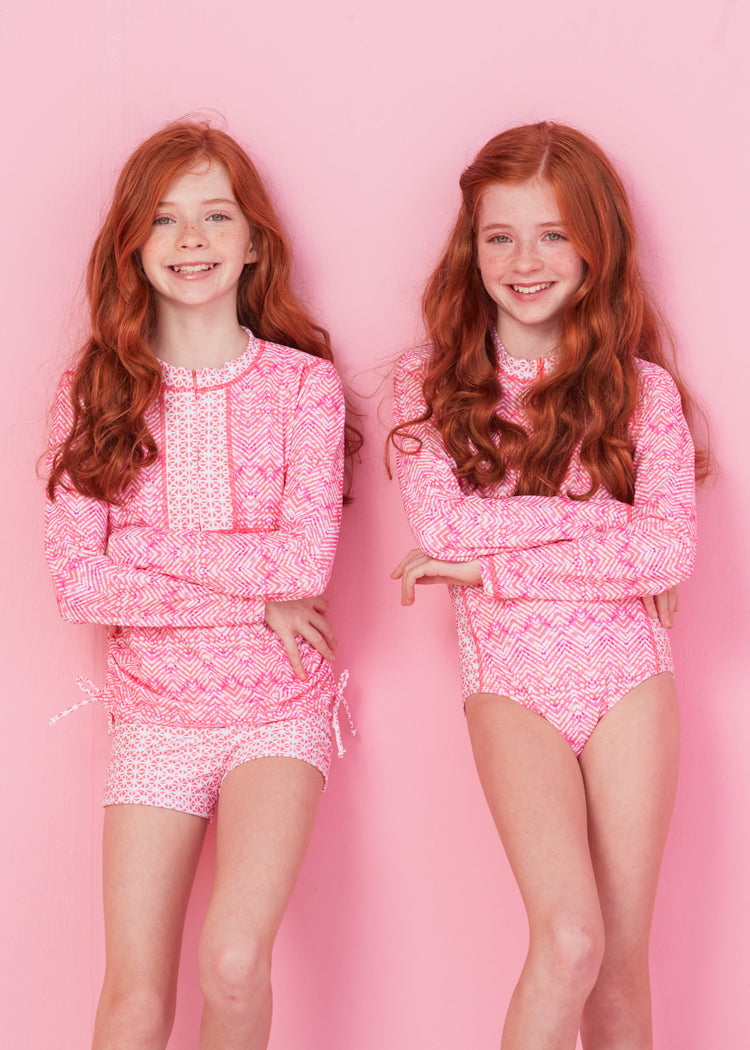 Twin redhead girls arms crossed on pink wall wearing Girls Algarve 3-Piece Long Sleeve Rashguard Set and other in Girls Algarve Unisuit