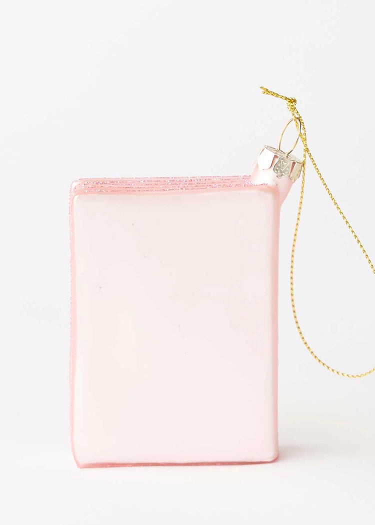 The back of a pink passport Christmas ornament with a gold string.