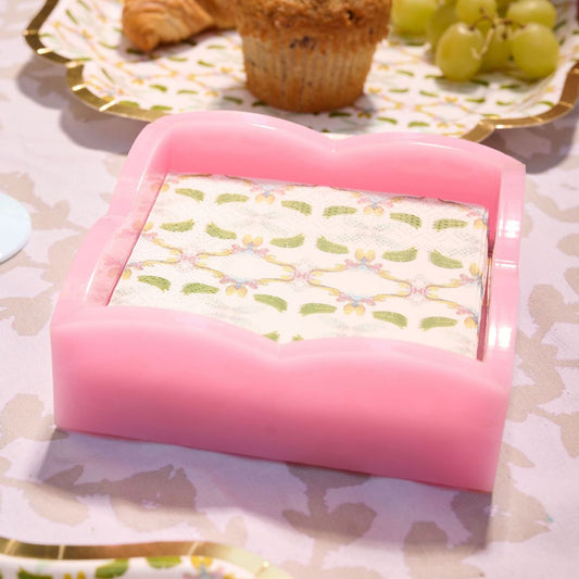 Pink napkin holder on a dining table with food in the background.