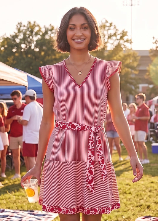 A woman wearing a red and white vertically striped dress with a red floral patterned waist tie belt, standing outdoors at a sunny summer event.