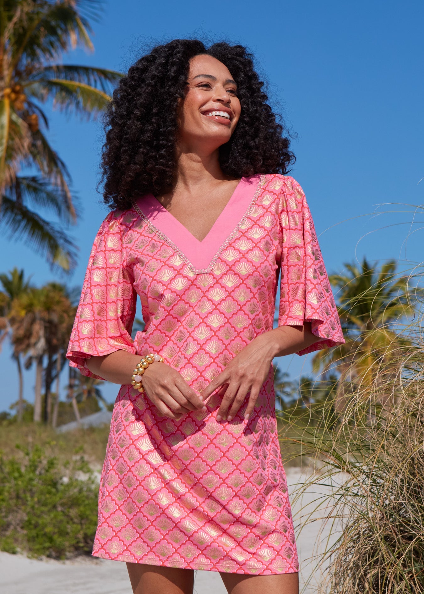 A woman with dark curly hair and arms crossed wearing the Coral Metallic Embroidered Flutter Sleeve Shift Dress on the beach.