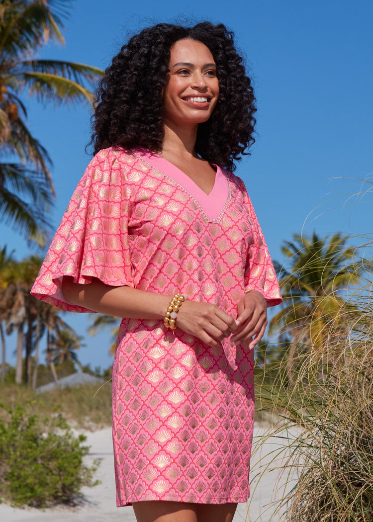 The side of a woman with her arms crossed smiling with dark curly hair wearing the Coral Metallic Embroidered Flutter Sleeve Shift Dress.