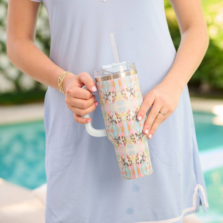 Person holding a colorful tumbler with a straw by a pool