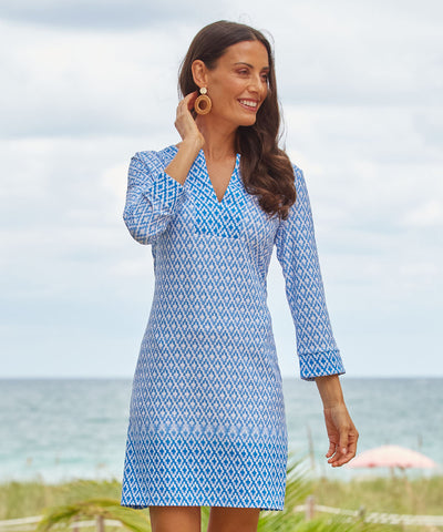 Woman wearing a blue and white printed dress with the ocean in the background.