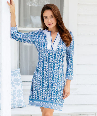 Woman wearing a blue and white printed dress with a white cottage in the background.