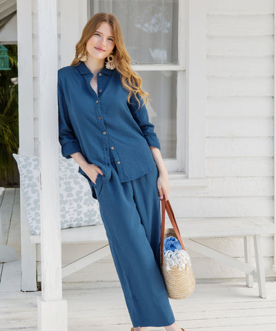 Woman wearing navy gauze pants and a matching top outside a white cottage.