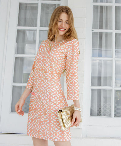 Woman wearing a white and pink printed metallic dress against a white wooden window.