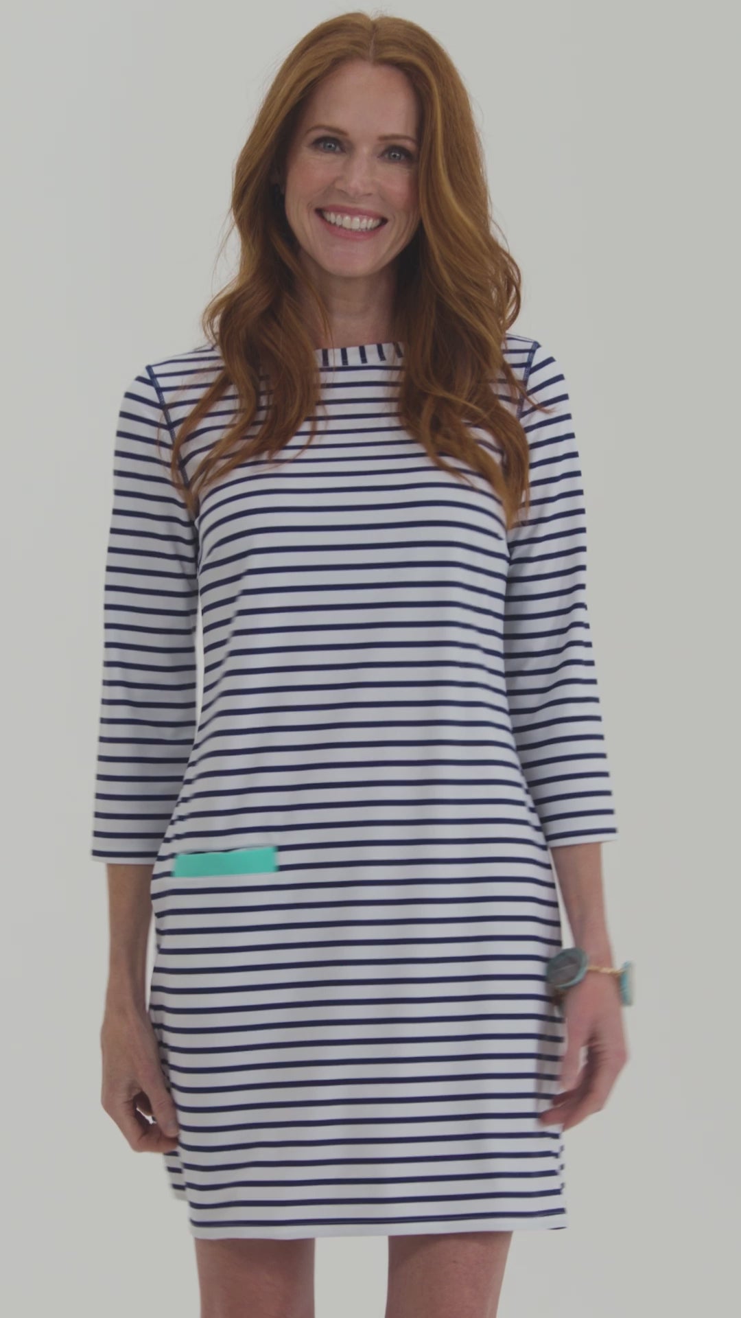 A redhead woman walking in and out of the frame wearing the Cabana Life sun protective Navy Stripe Cabana Shift Dress.