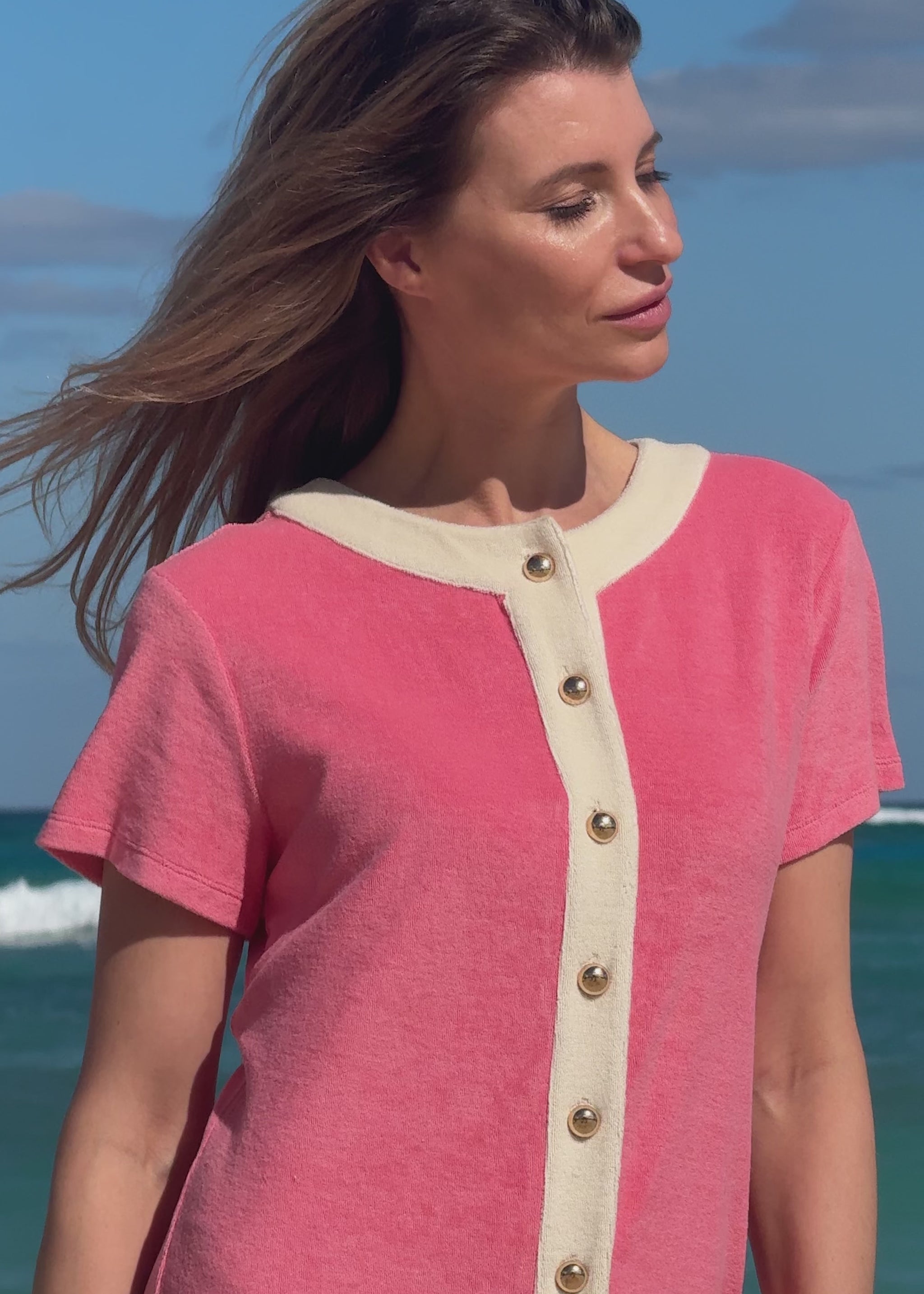 Woman wearing a pink terry dress with a blue sky and ocean background