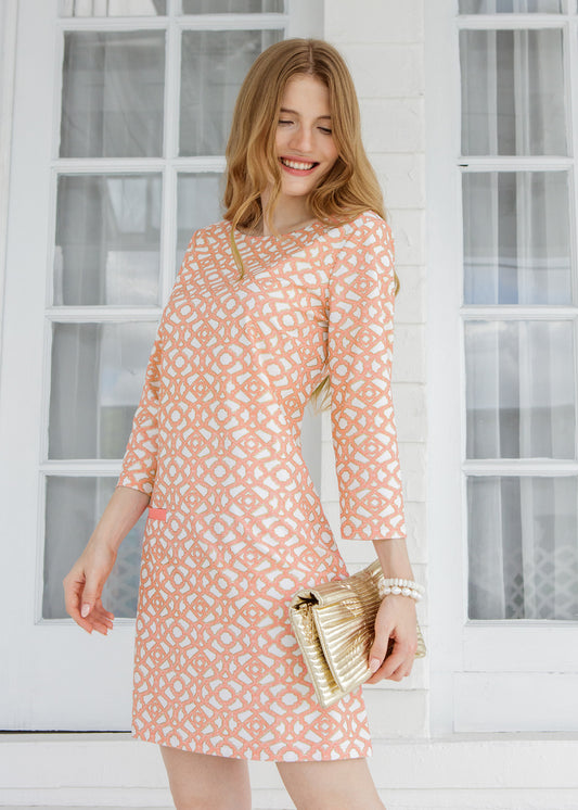 Woman wearing a patterned dress standing in front of a white window.