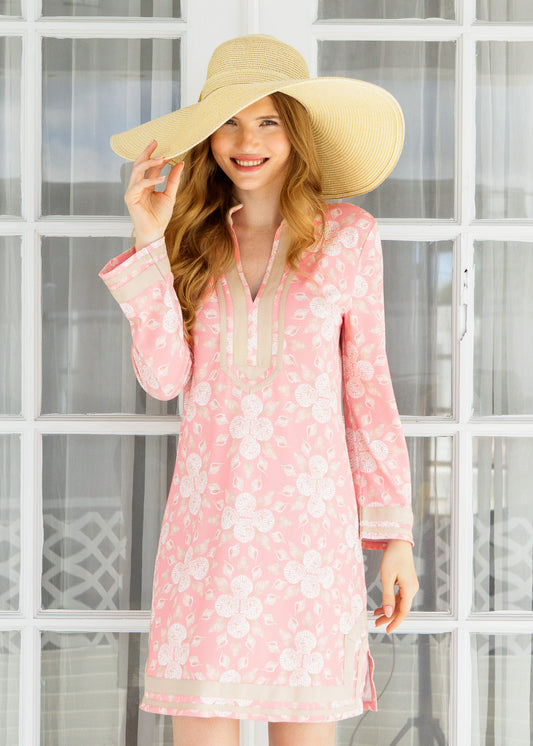 Woman wearing a pink seashell dress and beige hat in front of a glass door.