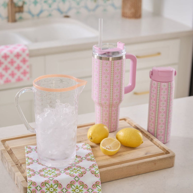 Pink insulated tumblers with a pitcher and lemons on a kitchen counter.