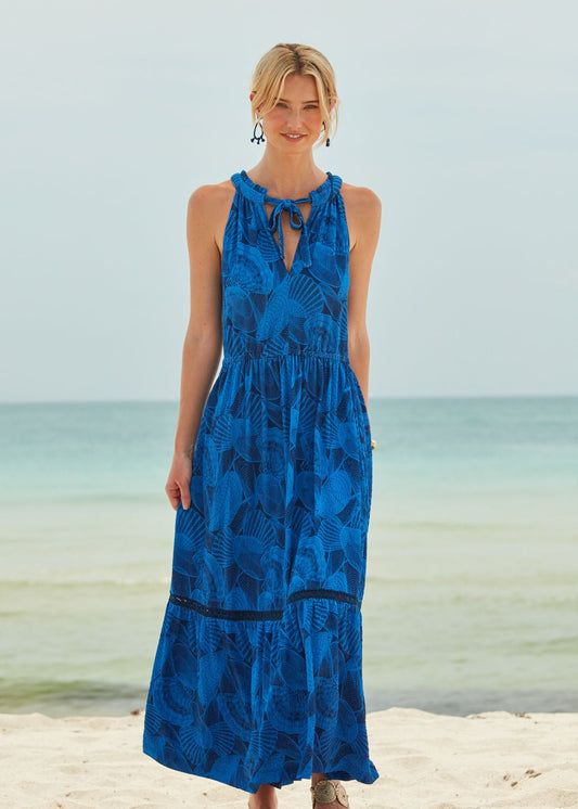 A blonde woman wearing the San Sebastian Tie Neck Maxi Dress standing on the beach.