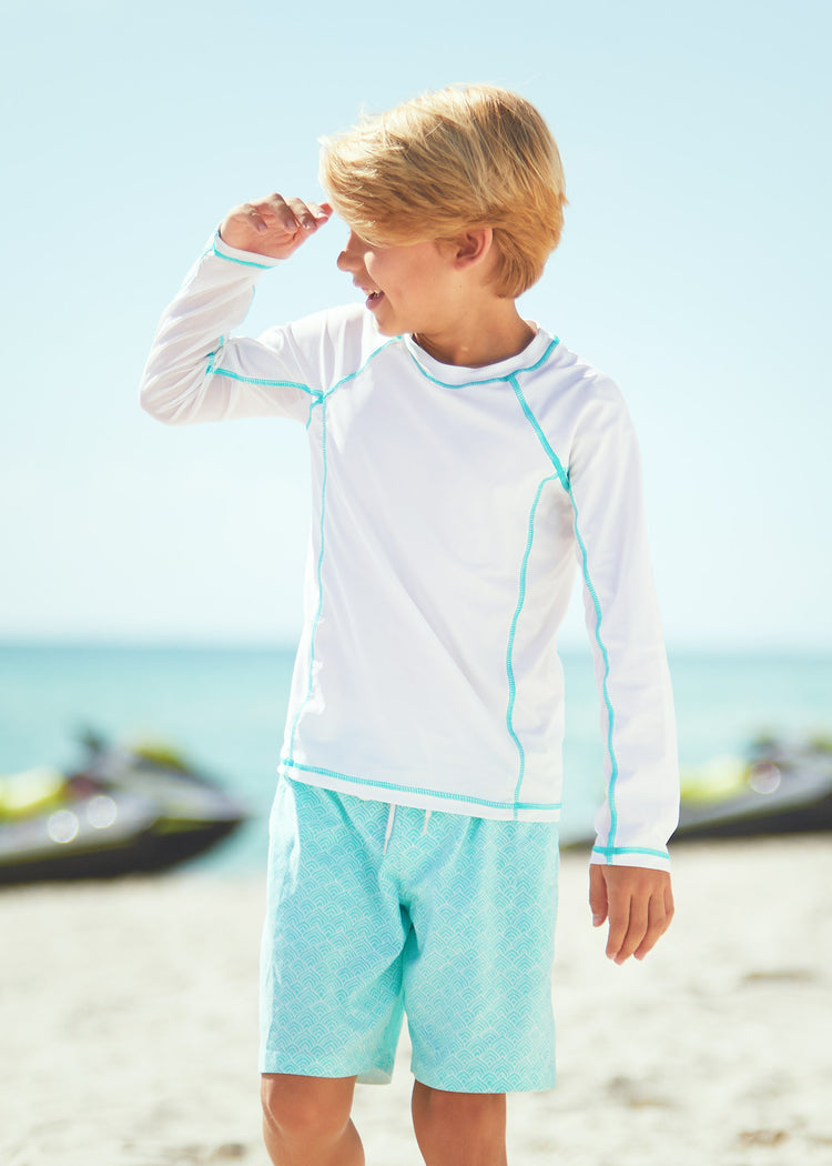 Boy walking on beach wearing Boys White Long Sleeve Rashguard with Boys Coral Tides Swim Trunks