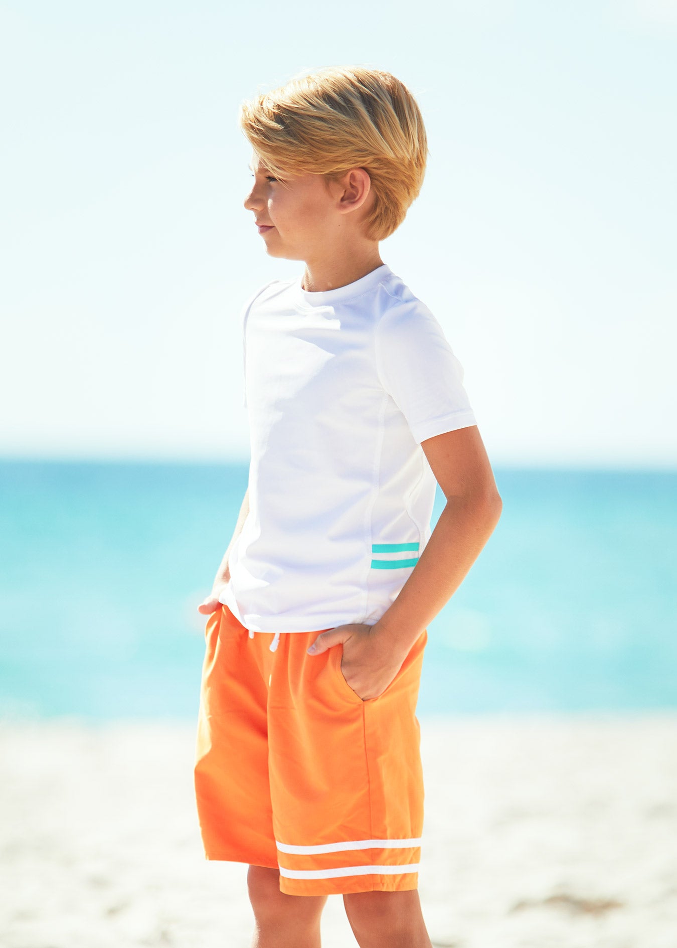 Boy on beach wearing Boys White Short Sleeve Rashguard with Boys Tangerine Swim trunks