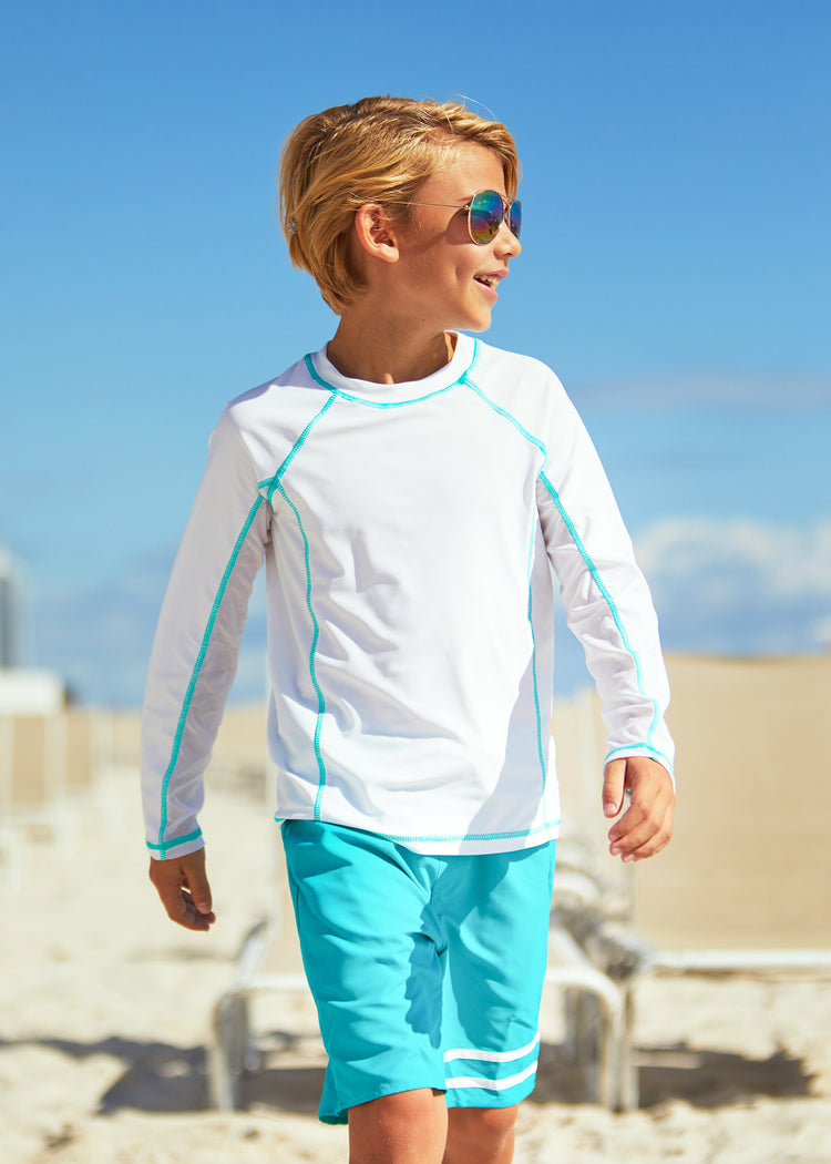 Boy walking on beach wearing Boys White Long Sleeve Rashguard with Boys Turquoise Swim Trunks