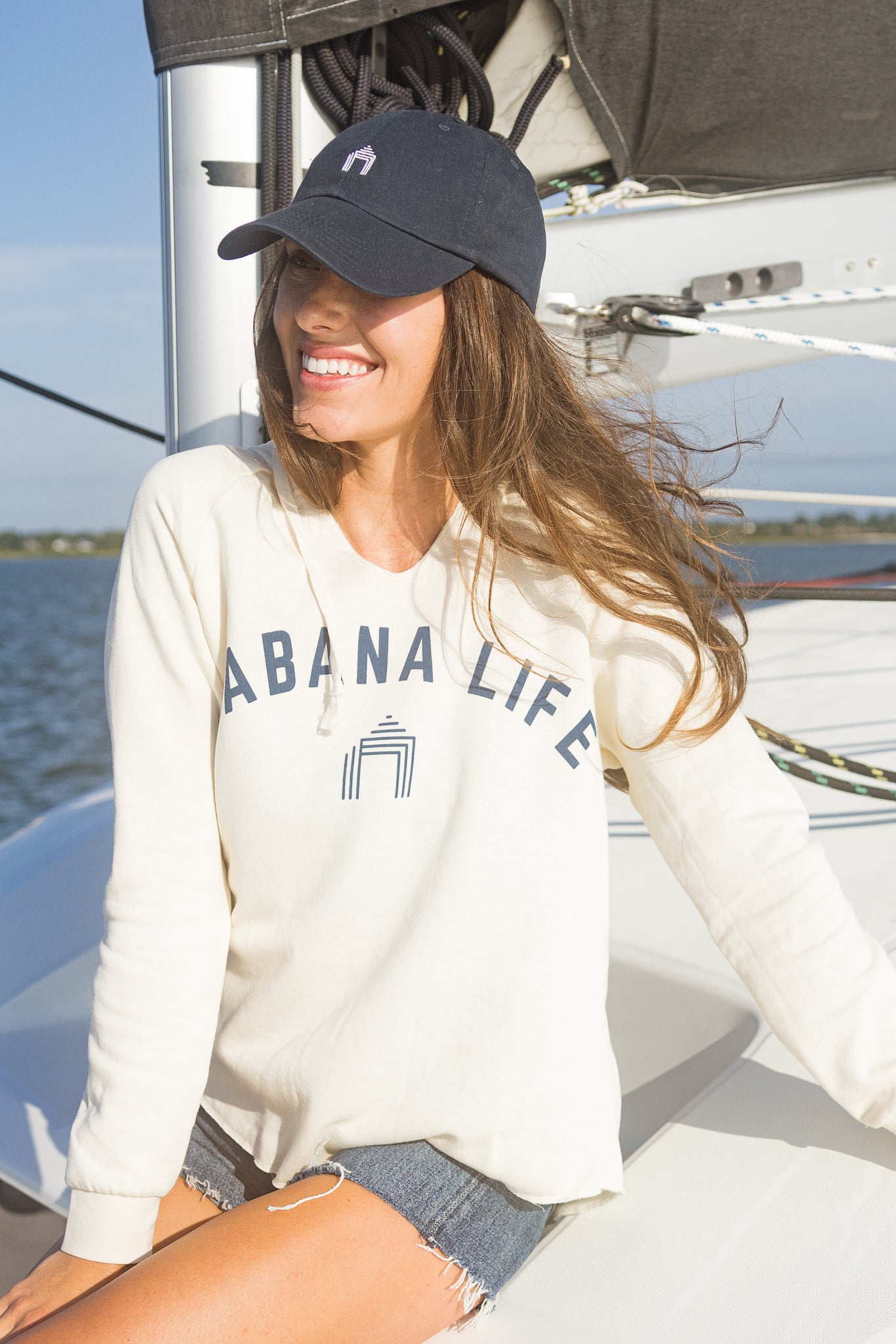 Woman wearing Cabana Life Navy Baseball Hat & Cabana Life Cream Hooded Sweatshirt